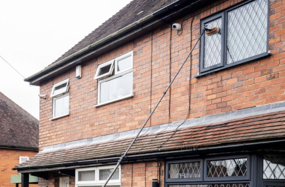 a window cleaner using an extended pole to clean an upstairs window on a house